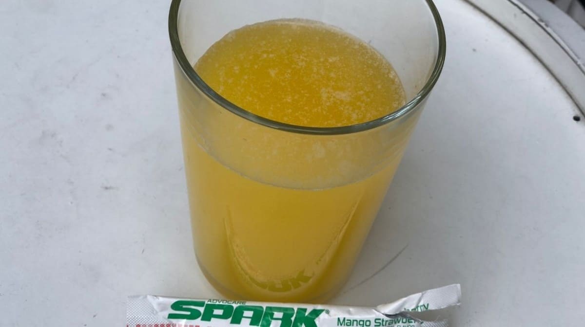 An Advocare Spark sachet in front of a glass with the drink mix inside