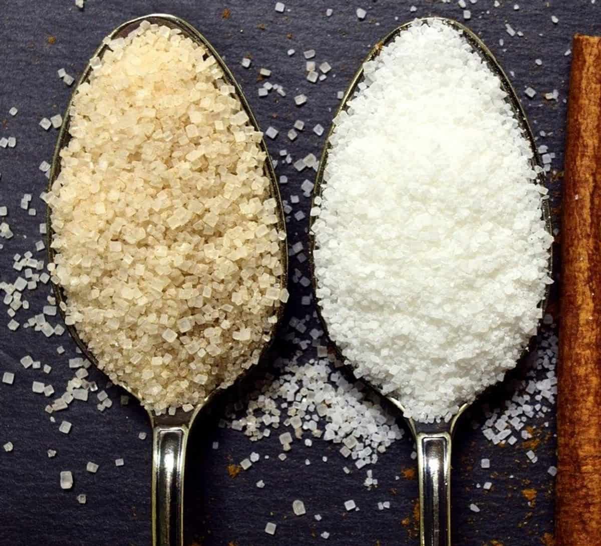 Brown and white sugar in two different spoons.